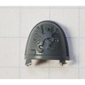 May include: Gray plastic miniature shoulder pad with a raised design of a winged lion.