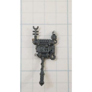 May include: A gray plastic model of a sci-fi weapon with a long, segmented barrel and a boxy, detailed body. The weapon has a small antenna on top and a series of pipes and wires.