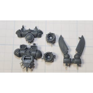 May include: A set of gray plastic miniature parts for a model kit. The parts include a chest piece, two wings, and two round pieces.