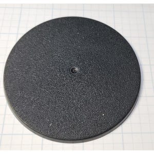 May include: A black round plastic base with a textured surface. The base has a small hole in the center.