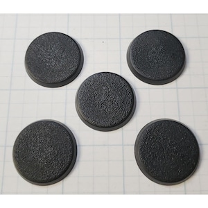 May include: Five black round plastic bases for miniature figures. The bases have a textured surface.