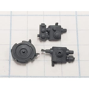 May include: Three small, gray plastic model kit parts are arranged on a white grid. The parts include a circular gear-like piece and two rectangular components with various protrusions and cylindrical features. The parts are likely for a model or miniature.