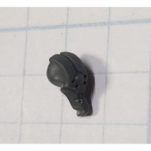 May include: A gray plastic miniature skull helmet with a detailed design. The helmet has a pointed top and a face mask with a skull design.