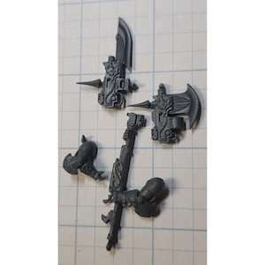 May include: Four gray plastic miniature figures with intricate details, resembling weapons or tools, for a tabletop game or hobby.