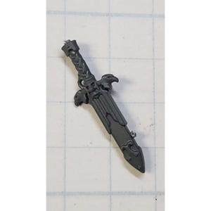 May include: A gray plastic miniature sword with a detailed design featuring two eagle heads and a decorative pattern. The sword has a pointed tip and a textured surface.