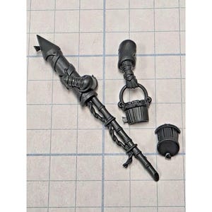 May include: Three unpainted black plastic miniature components consisting of a long spear with a pointed tip and wrapped handle, a separate hand holding a small bucket, and a small cylindrical cap piece with a flat top and ridged sides.