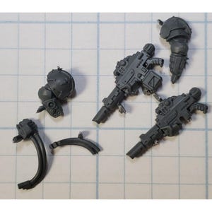 May include: A set of five gray plastic miniature figures for a tabletop game. The figures include two guns, a helmet, and two arms.
