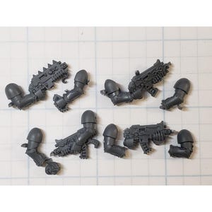 May include: Eight gray plastic miniature weapon parts for a tabletop wargame. The parts are for a futuristic weapon with a detailed design.