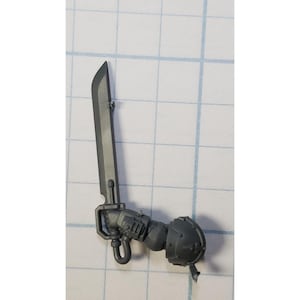 May include: A gray plastic miniature of a Space Marine's arm holding a power sword. The sword is a long, straight blade with a hilt and a power field.