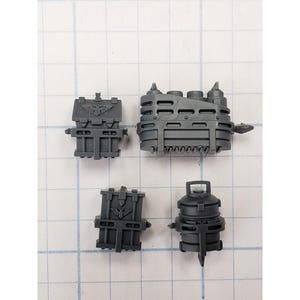 May include: Four gray plastic miniature components, likely for a model kit. The pieces include two rectangular boxes with an emblem, a cylindrical piece, and a larger, more complex component with multiple sections and details.
