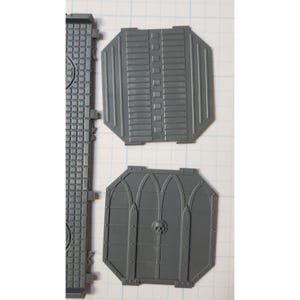 May include: Two gray plastic pieces for a model building kit. One piece has a grid pattern and the other has a skull and gothic arch design.