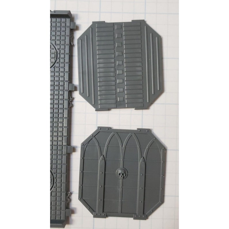 May include: Two gray plastic pieces for a model building kit. One piece has a grid pattern and the other has a skull and gothic arch design.