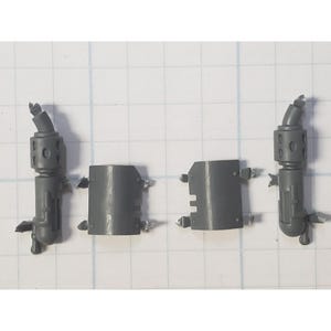 May include: Four gray plastic model kit components are arranged on a grid background. Two are cylindrical with a curved top and multiple holes. The other two are rectangular with tabs. These appear to be miniature model parts.