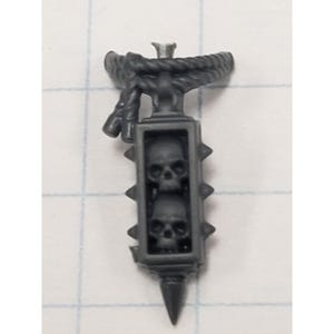May include: A dark gray miniature weapon featuring a rectangular cage with two skulls, surrounded by spikes. A rope detail is at the top, and a pointed tip at the bottom. This item is likely for a tabletop game.
