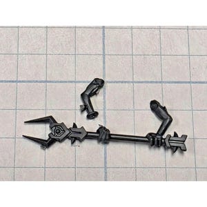 May include: A black plastic miniature component featuring a long staff with a three-pronged head and a decorative center, accompanied by a separate arm piece with a hand gripping the staff and a detached arm piece with a rounded shoulder joint.