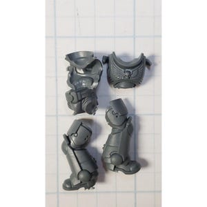 May include: A collection of gray plastic miniature model parts, including a torso piece with a skull and wing emblem, two leg pieces, and a backpack component. The pieces are designed for assembly and are likely for a tabletop game.