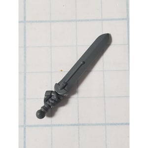 May include: A gray plastic miniature sword with a detailed handle and a straight blade. The handle features a textured grip and a rounded pommel. The sword is designed for tabletop gaming or model building.