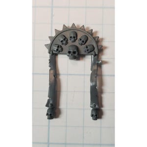 May include: Gray plastic model kit of a skull-topped archway with seven skulls. The archway is made of two vertical pieces with a curved top piece. The skulls are all facing forward.