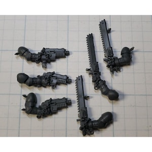 May include: Six gray plastic miniature weapons for a tabletop war game. The weapons include chain swords and chain guns.