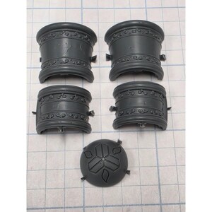 May include: Four dark gray curved plastic components featuring embossed scrollwork patterns along the top and bottom edges, accompanied by one circular dark gray plastic piece with a central three-part geometric design and small protruding tabs.