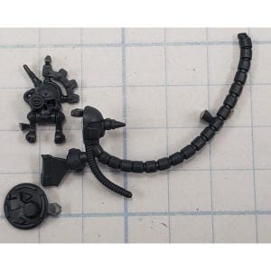 May include: A collection of black plastic model kit parts. The components include a skull-shaped piece with gears, a segmented tube, a circular piece, and other mechanical elements. The parts are designed for assembly and are likely for a miniature model.