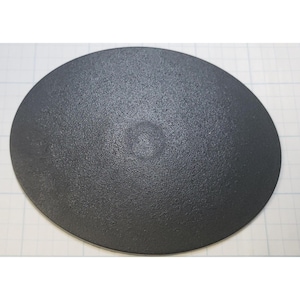 May include: A solid black, oval-shaped object with a textured surface. The object is centered in the frame and appears to be made of a matte material. The background is a white surface with a grid pattern.