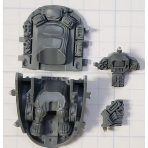 May include: A set of gray plastic model pieces for a robot or vehicle. The pieces are detailed with raised lines and small squares.