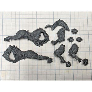 May include: A collection of dark gray plastic model kit components featuring textured fur-like surfaces, including two large body sections, a curved tail piece, several smaller limb segments, and a mechanical arm attachment with a weapon.