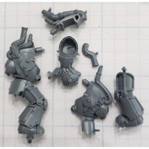 May include: A collection of unassembled, gray plastic miniature parts, likely for a model kit. The components include a leg, torso, helmet, and various mechanical attachments. The pieces are arranged on a grid-lined surface, suggesting a hobby or crafting theme.