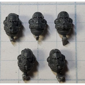May include: Five gray plastic miniature heads with detailed facial features and helmets. The heads are for use in a tabletop wargame.