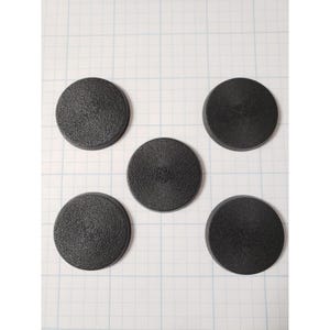 May include: Five black, circular objects with a textured surface are arranged on a grid background. The objects appear to be made of a solid material and have a slightly raised center.