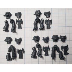 May include: A collection of unpainted, gray plastic miniature parts, including helmets, shoulder pads, and leg armor. These components appear to be for assembling a miniature figure, likely for tabletop gaming or hobby projects.