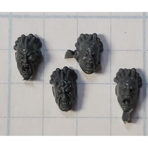 May include: Four grey plastic miniature heads with detailed facial features and hair. The heads are for use in tabletop games or model building.