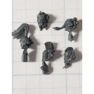 May include: Five grey plastic miniature heads with different hairstyles and facial features. The heads are for use in a tabletop wargame.