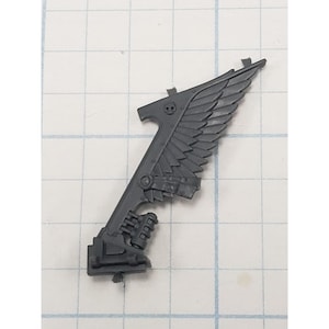 May include: A gray plastic miniature wing with a skull emblem, part of a model kit. The wing features detailed feathering and mechanical elements, typical of science fiction or fantasy miniatures.