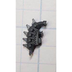 May include: A small, dark gray plastic component with a complex, mechanical design. It features multiple interlocking sections, a ridged tube, and several protruding, stylized spikes. The object appears to be a piece of a larger assembly.