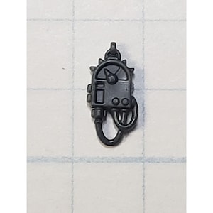 May include: A black plastic miniature of a device with a dial, buttons, and a cord. The device has a spiky, circular design around the dial.