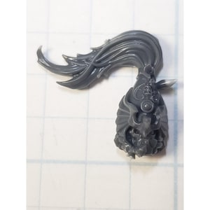 May include: A gray plastic miniature figure component, possibly for a tabletop game. The piece features a detailed, stylized design with flowing, flame-like elements and a textured, ornate head.