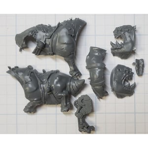 May include: A set of gray plastic miniature figures for a tabletop game. The figures are of a creature with a large head and a body that is partially covered in armor. The figures are in various poses, including standing, running, and attacking.