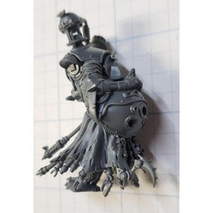 May include: A gray plastic miniature figure featuring a mechanical torso with a rounded, bulbous midsection, a helmeted head, and a tattered, flowing lower garment. The figure includes intricate robotic details, multiple protruding appendages, and a long, thin staff-like component extending from the back.