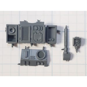 May include: A collection of unpainted, gray plastic model kit parts. The components include a rectangular box with hinged doors, a panel with a circular vent, and several cylindrical and box-shaped pieces. The parts are arranged on a grid background.