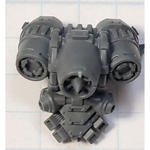 May include: A gray plastic miniature jetpack component featuring three prominent circular thrusters, a central engine housing with a pointed nozzle, and a lower section with four smaller rectangular exhaust vents, designed for tabletop gaming models.