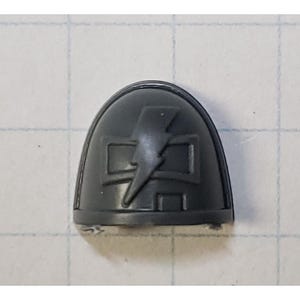 May include: A gray plastic shoulder pad with a raised design of a lightning bolt and a square frame.