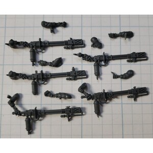 May include: A set of seven gray plastic miniature weapons for a tabletop wargame. The weapons are detailed with intricate designs and have a futuristic aesthetic.