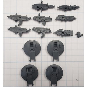May include: A set of 10 grey plastic miniature parts for a model kit. The parts include guns, shields, and other accessories.