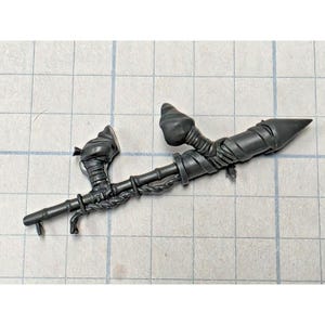 May include: A dark gray plastic miniature weapon component featuring a long, slender shaft with a pointed tip, wrapped in textured cord details. The piece includes two distinct, bulbous, organic-shaped protrusions attached to the main rod.