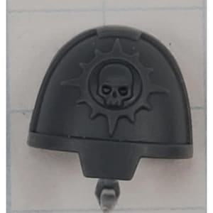 May include: A gray plastic shoulder pad with a skull and sunburst emblem. The emblem is centered on the pad and features a detailed skull within a stylized sun. The shoulder pad has a curved shape and a small peg extending from the bottom.