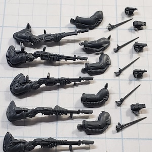May include: A collection of unpainted, gray plastic miniature weapon and armor components. The set includes five long rifles, five seats, five small side arms, and five additional pieces. The parts are arranged on a grid.