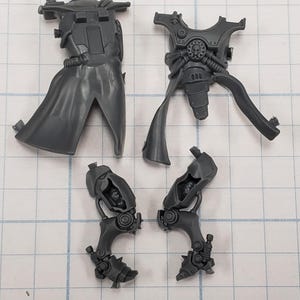 May include: A collection of unpainted, gray plastic miniature model parts. The components include a torso with a cape, a chest piece with mechanical details, and two leg assemblies with intricate designs, likely for a tabletop game.