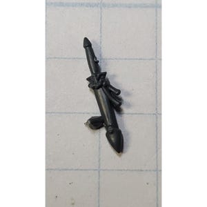 May include: A gray plastic miniature of a spear with a tied-on cloth. The spear is pointed at the tip and has a small handle.